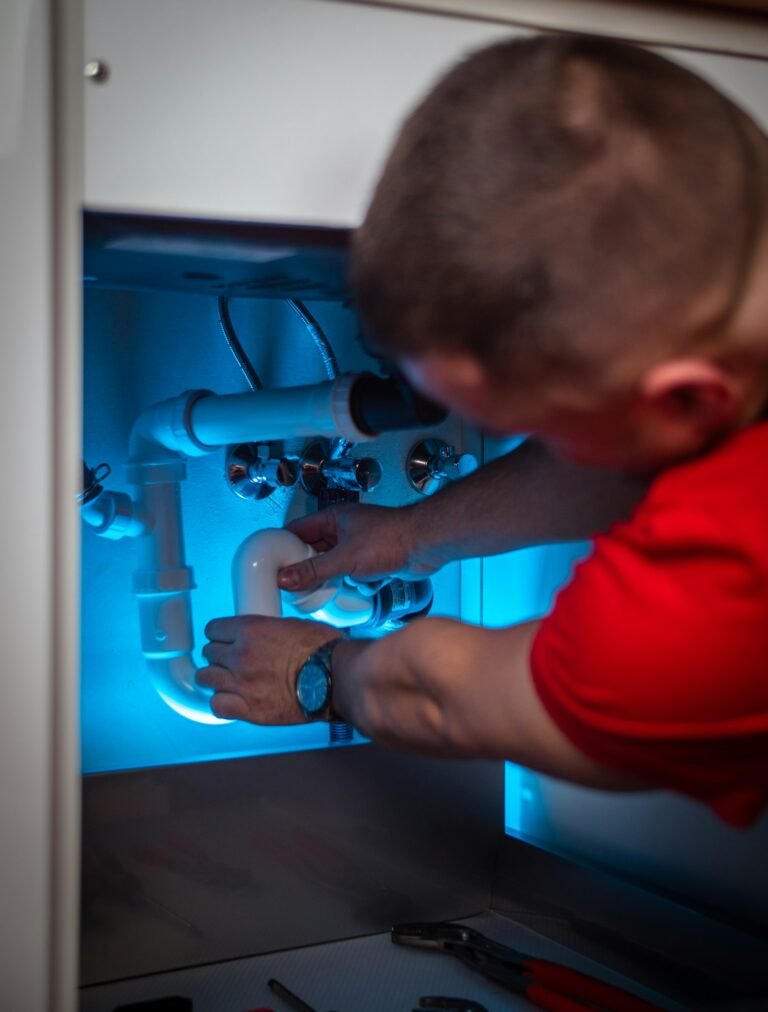 Plumber working on drain pipes under a sink during a Peoria Heights service call
